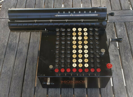 Monroe Model G mechanical calculator. It has a full keyboard with red reset buttons at the bottom of each row, and has a shiny black finish.