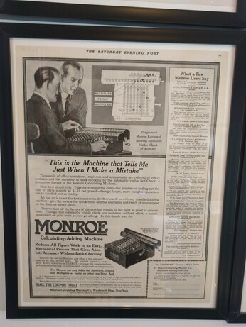 A vintage ad from a 1918 issue of the Saturday Evening Post. It shows two men in front of a Monroe Model G mechanical calculator. The tagline on the ad reads "This is the Machine that Tells Me Just When I Make a Mistake."