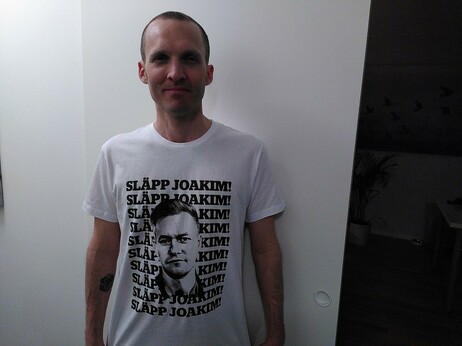 Bild på mig med en t-shirt. Det står SLÄPP JOAKIM flera rader som bakgrund med svarta bokstäver . En svartvit bild på Joakim i förgruunden
